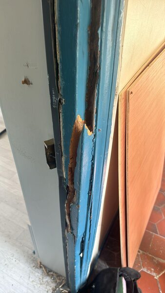 dormant de porte bleu fortement endommagé autour de la serrure après effraction, gâche métallique visible