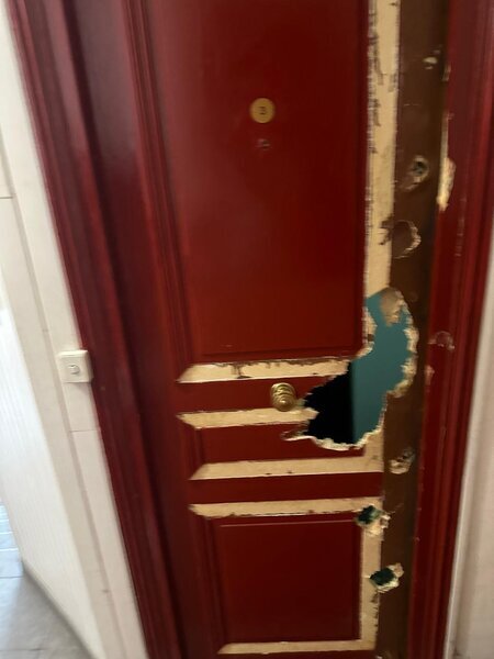 Porte d'entrée rouge perforée après effraction, serrure et bâti endommagés, intervention serrurier recommandée