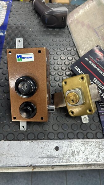 Serrure en applique Mottura démontée avec barillet laiton et pêne posés sur un établi antidérapant.